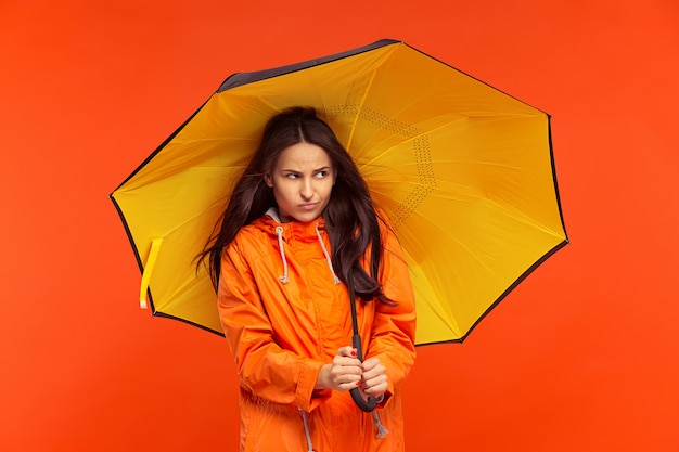 La joven posando en el estudio en chaqueta de otoño aislada en rojo. Emociones humanas negativas. Concepto de clima frío. Conceptos de moda femenina