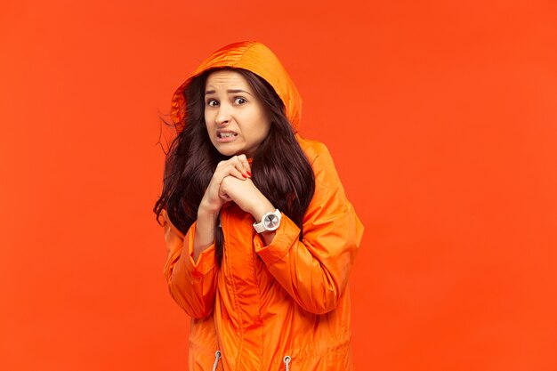 La joven posando en el estudio en chaqueta de otoño aislada en rojo. Emociones humanas negativas. Concepto del clima frío