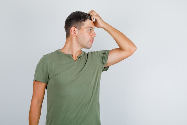 Joven posando con la mano en la cabeza en camiseta verde militar y mirando elegante, vista frontal.