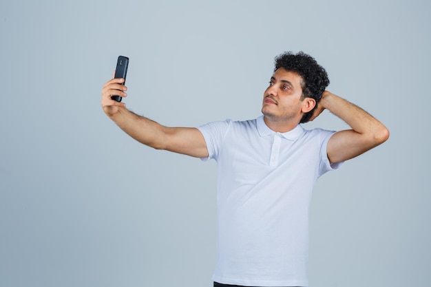 Joven posando mientras toma selfie en camiseta blanca y se ve lindo. vista frontal.