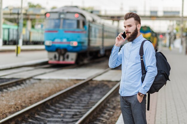 Joven, posición, en, estación del ferrocarril, utilizar, teléfono celular