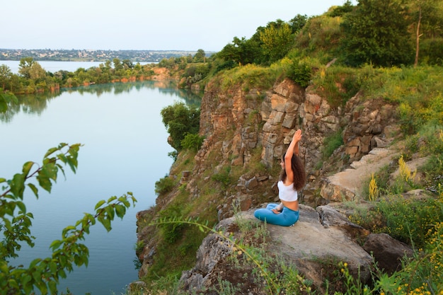 Joven practica yoga cerca del río