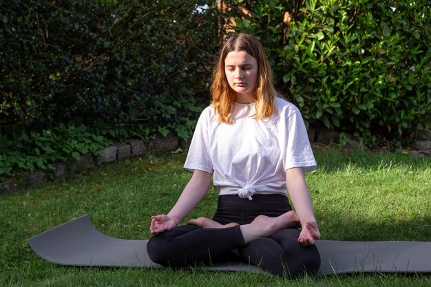 Una joven practica yoga en la naturaleza en el césped del patio.