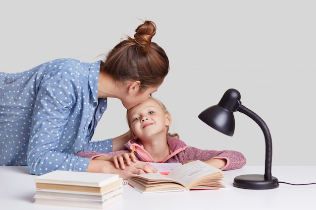 La joven se preocupa por su hijo, besa a su hija en la frente, la alaba para que estudie bien, explica el material, lee libros y se prepara para las lecciones en la escuela, aislado en blanco. Concepto de estudio