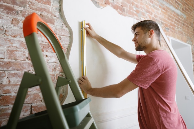 Foto gratuita joven preparándose para hacer reparaciones de apartamentos por él mismo. antes de la remodelación o renovación de la casa. concepto de relaciones, familia, bricolaje. medir la pared antes de pintar o diseñar.