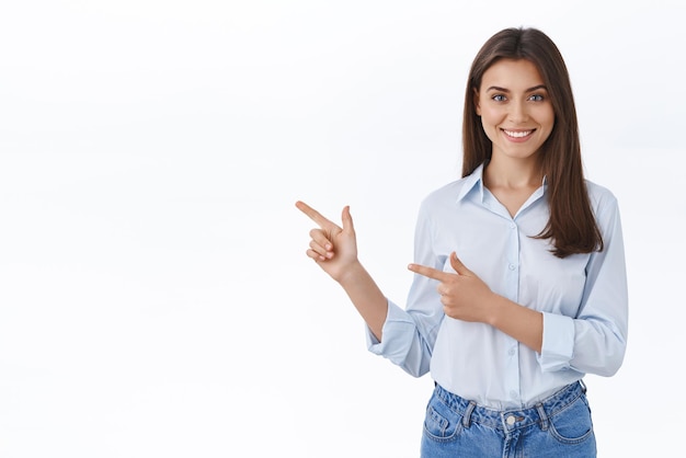 Una joven profesional y sonriente ayuda al cliente a encontrar dónde ir mostrando el camino que señala con el dedo a la izquierda y sonríe amablemente complacido de responder cualquier pregunta mientras presenta un nuevo producto de fondo blanco.