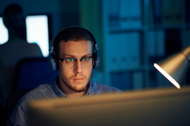 Joven programador en gafas y auriculares trabajando en oficina