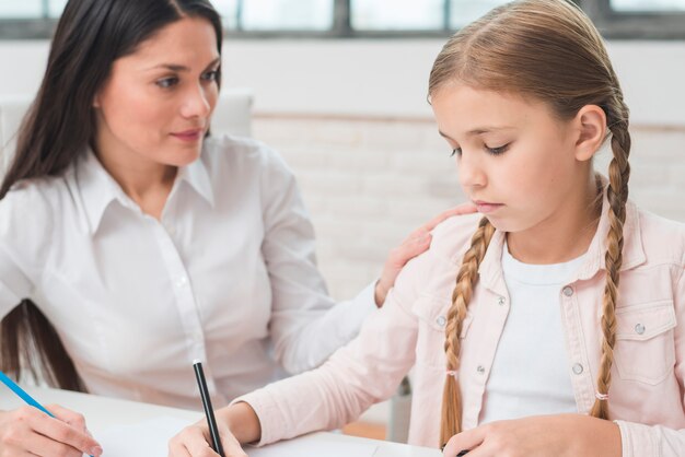 Joven psicóloga consolando a la niña triste dibujando con rotuladores.