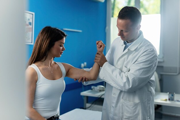 Una joven que le examina el brazo y el codo con una cita médica con un ortopedista masculino en la clínica