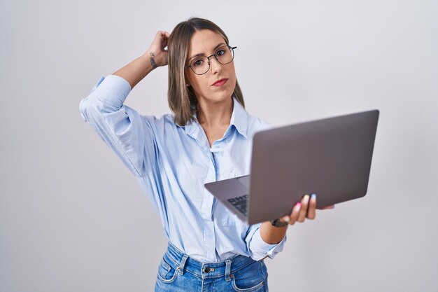 Una joven que trabaja usando una computadora portátil se confunde y se pregunta sobre la pregunta. incierto con la duda, pensando con la mano en la cabeza. concepto pensativo.