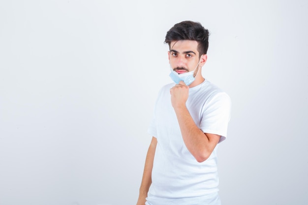 Joven quitándose la máscara con camiseta blanca y mirando confiado