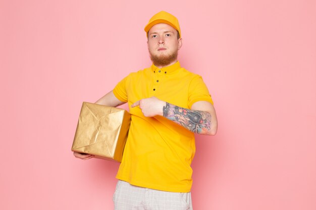 joven repartidor en polo amarillo gorra amarilla jeans blancos sosteniendo una caja en rosa