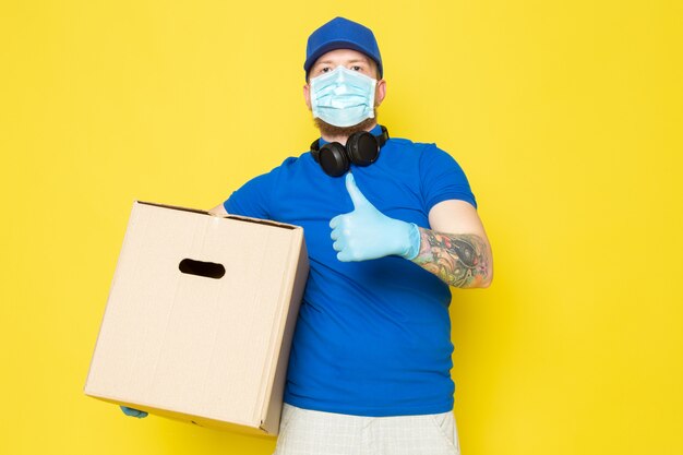 joven repartidor en polo azul gorra azul jeans blancos mochila con cajas en amarillo