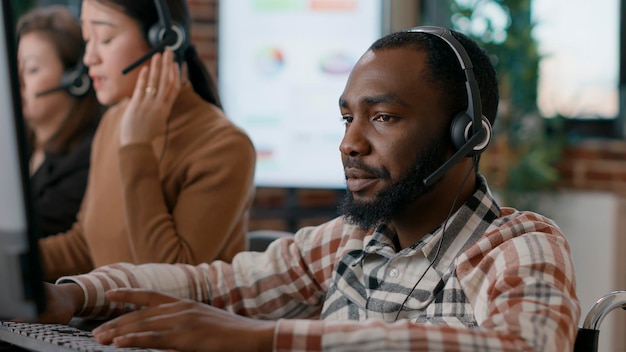 Joven respondiendo llamadas de teletrabajo en el trabajo de servicio al cliente, hablando con clientes en la línea de ayuda telefónica. Trabajador masculino que usa auriculares de audio para brindar asistencia y apoyo a las personas. De cerca.