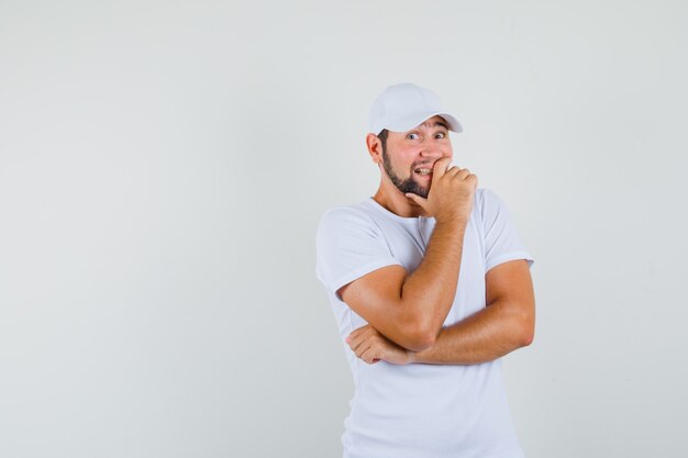 Joven riendo con la mano en la camiseta, gorra y mirando alegre, vista frontal. espacio para texto