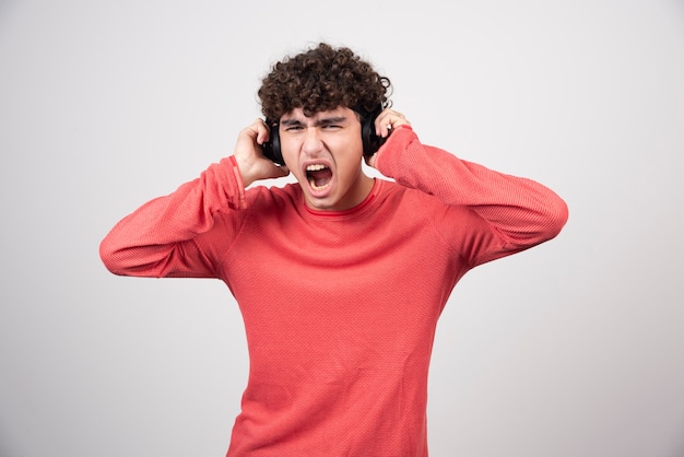 Joven rizado con auriculares escuchando canciones con volumen alto.