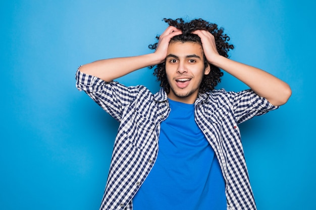 Joven rizado manos arriba aislado en la pared azul