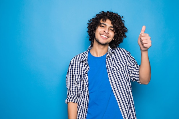 Foto gratuita joven rizado con pulgares arriba aislado en la pared azul