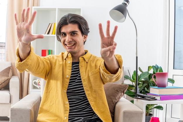 Joven en ropa casual mirando sonriendo alegremente mostrando el número ocho sentado en la silla en la sala de luz