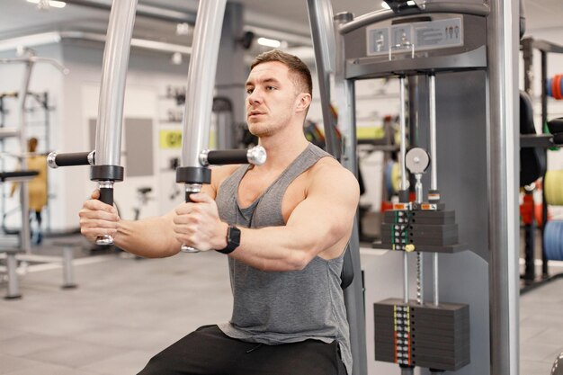 Joven en ropa deportiva haciendo ejercicios en equipos especiales en el gimnasio