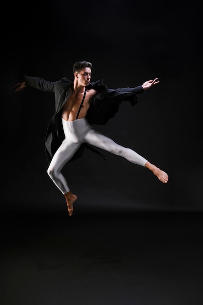 Joven en ropa elegante saltando y bailando sobre fondo negro