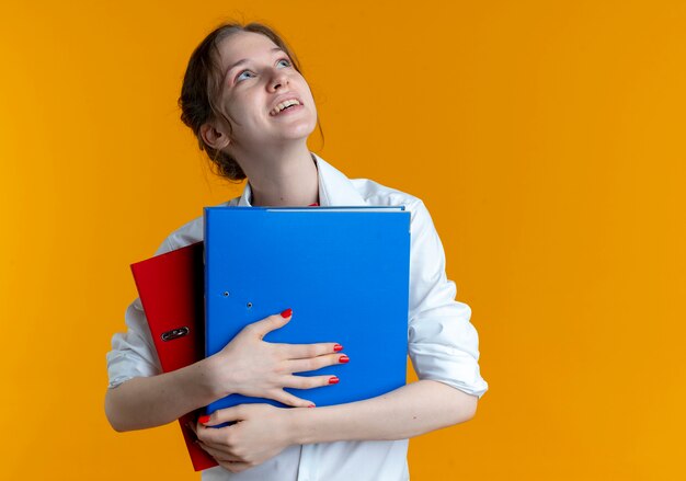 joven rubia alegre chica rusa tiene carpetas de archivos mirando hacia arriba