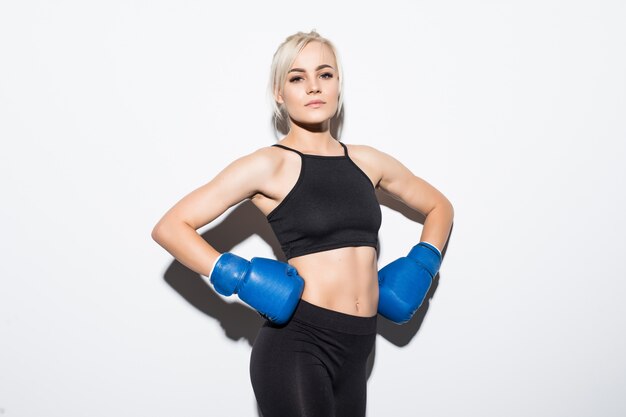 Joven rubia con guantes de boxeo azules preparada para ganar en blanco