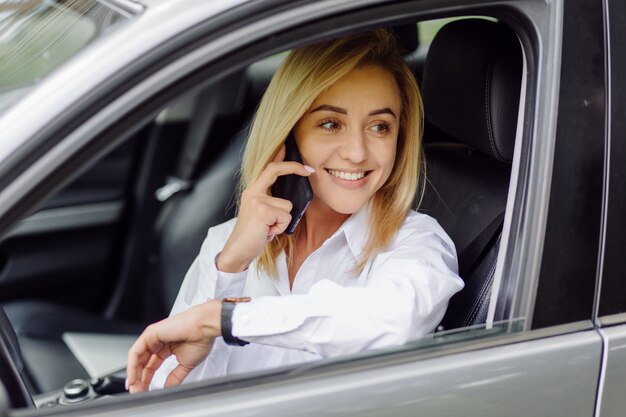 Joven rubia hermosa dentro del auto con teléfono