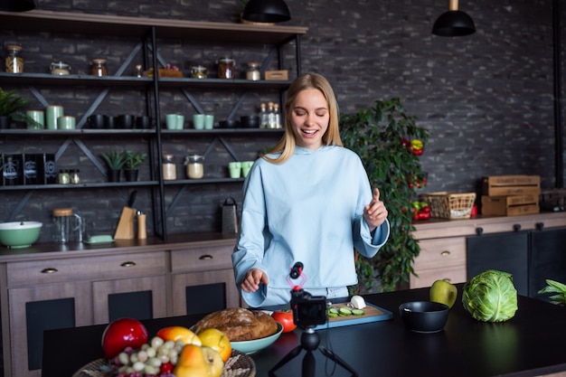 Joven rubia hermosa toma videos mientras cocina en la cocina