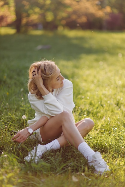 Joven rubia lleva una sudadera con capucha blanca sonriendo y caminando en el bosque