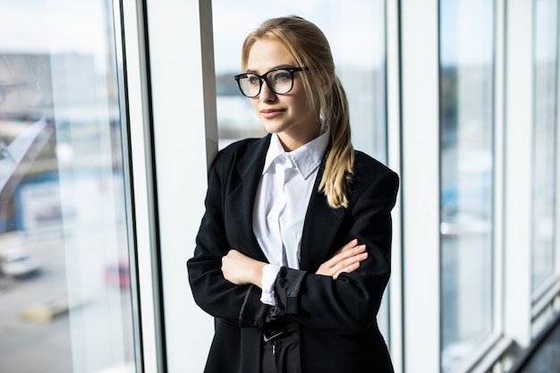 Joven rubia con las manos cruzadas está de pie en la oficina panorámica de la esquina.