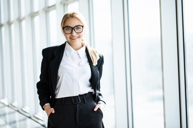 Joven rubia con las manos cruzadas está de pie en la oficina panorámica de la esquina.