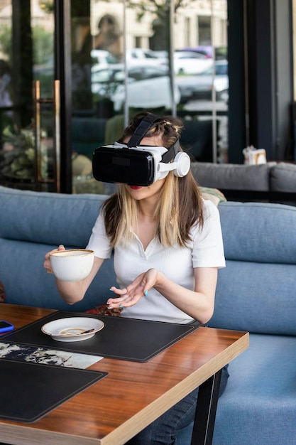 Joven rubia con set de realidad virtual y bebiendo café en el restaurante