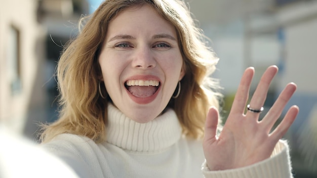 Joven rubia sonriendo confiada teniendo videollamada en la calle