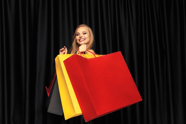 Joven rubia en vestido de compras sobre fondo negro. Atractiva modelo de mujer caucásica.