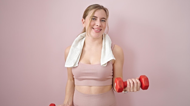 Foto gratuita joven rubia vistiendo ropa deportiva entrenando con pesas sobre un fondo rosa aislado