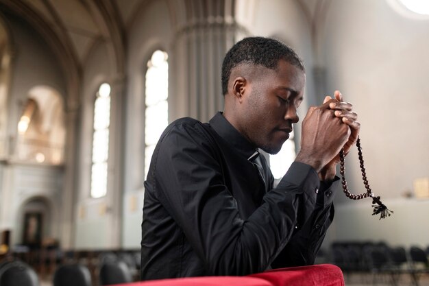 Joven sacerdote masculino rezando en la iglesia con rosario