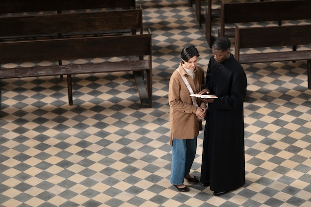 Joven sacerdote y mujer hablando en la iglesia mientras sostiene una biblia