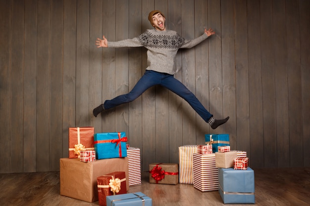 Joven saltando de alegría entre los regalos de Navidad sobre pared de madera