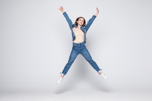 Joven saltando en jeans en pared blanca