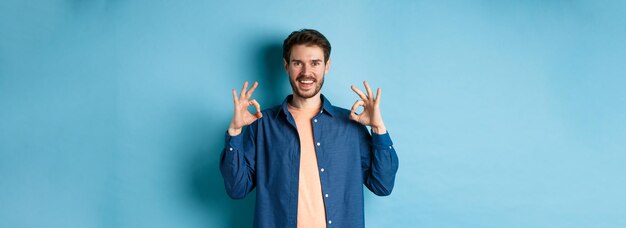 Un joven satisfecho sonriendo y mostrando un gesto correcto aprueba algo bueno alabando algo excelente