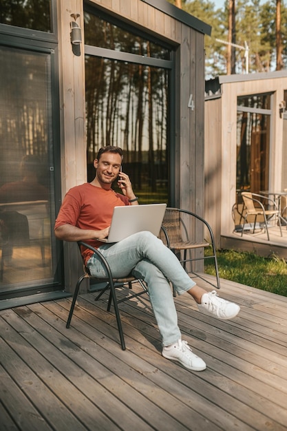 Foto gratuita un joven sentado afuera y hablando por teléfono.