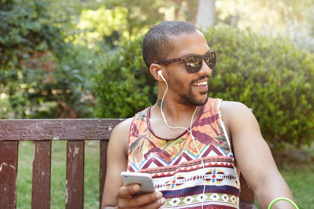 Joven sentado en un banco en el parque y escuchando música