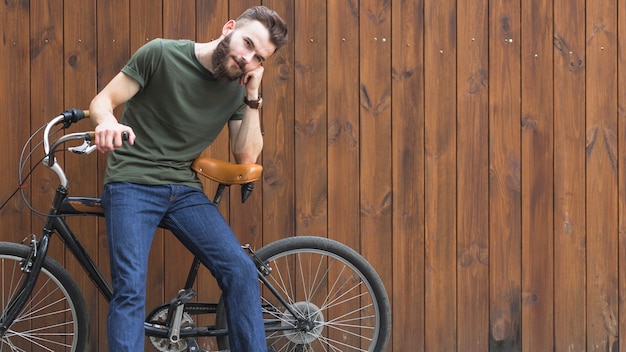 Joven sentado en bicicleta contra el fondo de madera