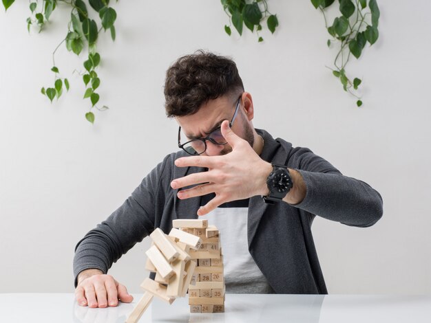 Joven sentado en gafas relojes chaqueta gris crushiing pequeña construcción de madera junto con planta en blanco