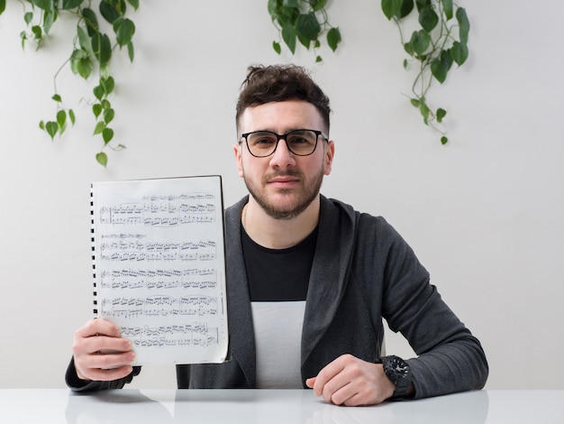 Joven sentado en gafas relojes chaqueta gris con cuaderno con notas junto con planta en blanco