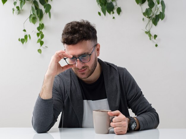 joven sentado en gafas relojes chaqueta gris junto con planta en blanco