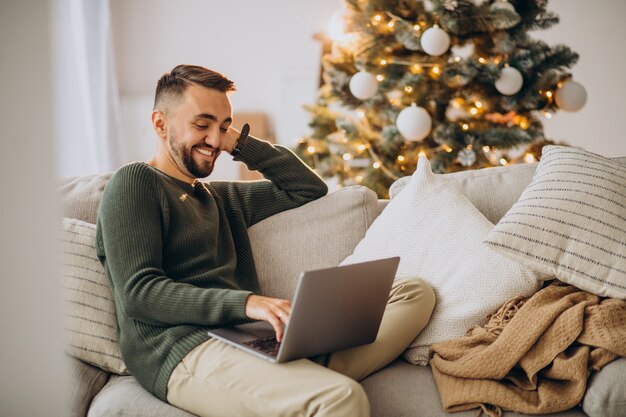 Joven sentado en el sofá y usando la computadora portátil en Navidad