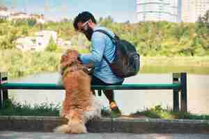 Foto gratuita joven sentado con su perro en la silla en el parque