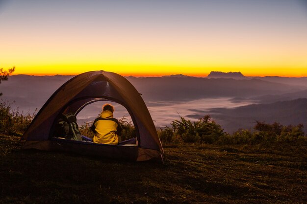 Un joven sentado en la tienda mirando el paisaje de montaña en invierno